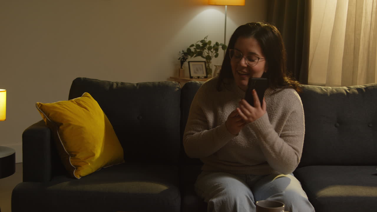 mujer joven pasando la noche en casa sentada en el sofá respondiendo a una llamada en el teléfono móvil