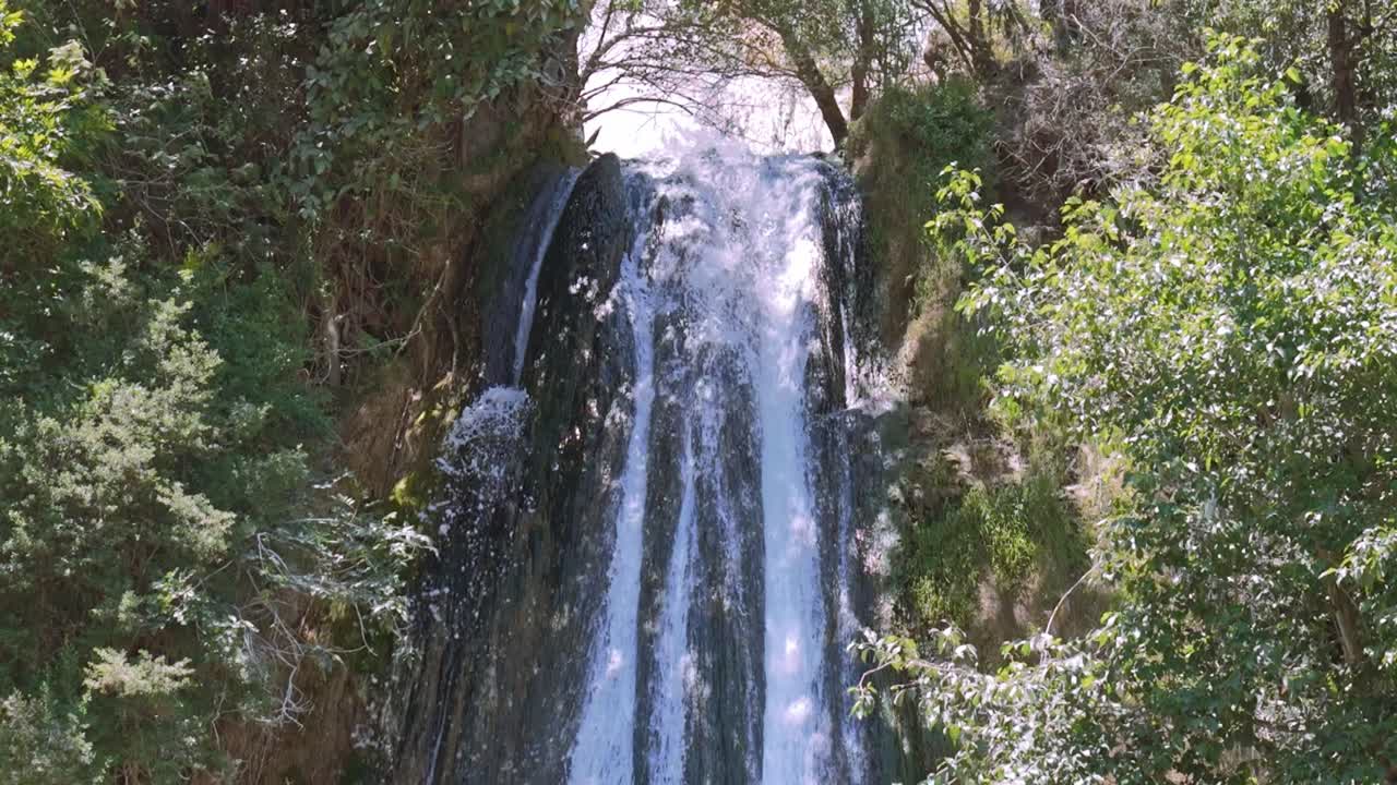 Waterfall cascading down in a lush green landscape, surrounded by trees and vibrant nature, slow motion