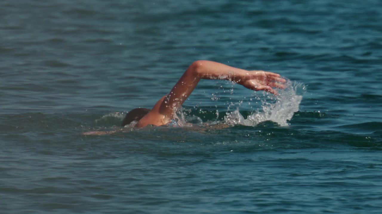 Hombre nadando estilo libre, disfrutando de un refrescante chapuzón en el océano en un día soleado y brillante. Ocio activo y deporte