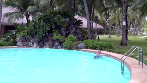 a man relaxes in the outdoor pool next to a waterfall