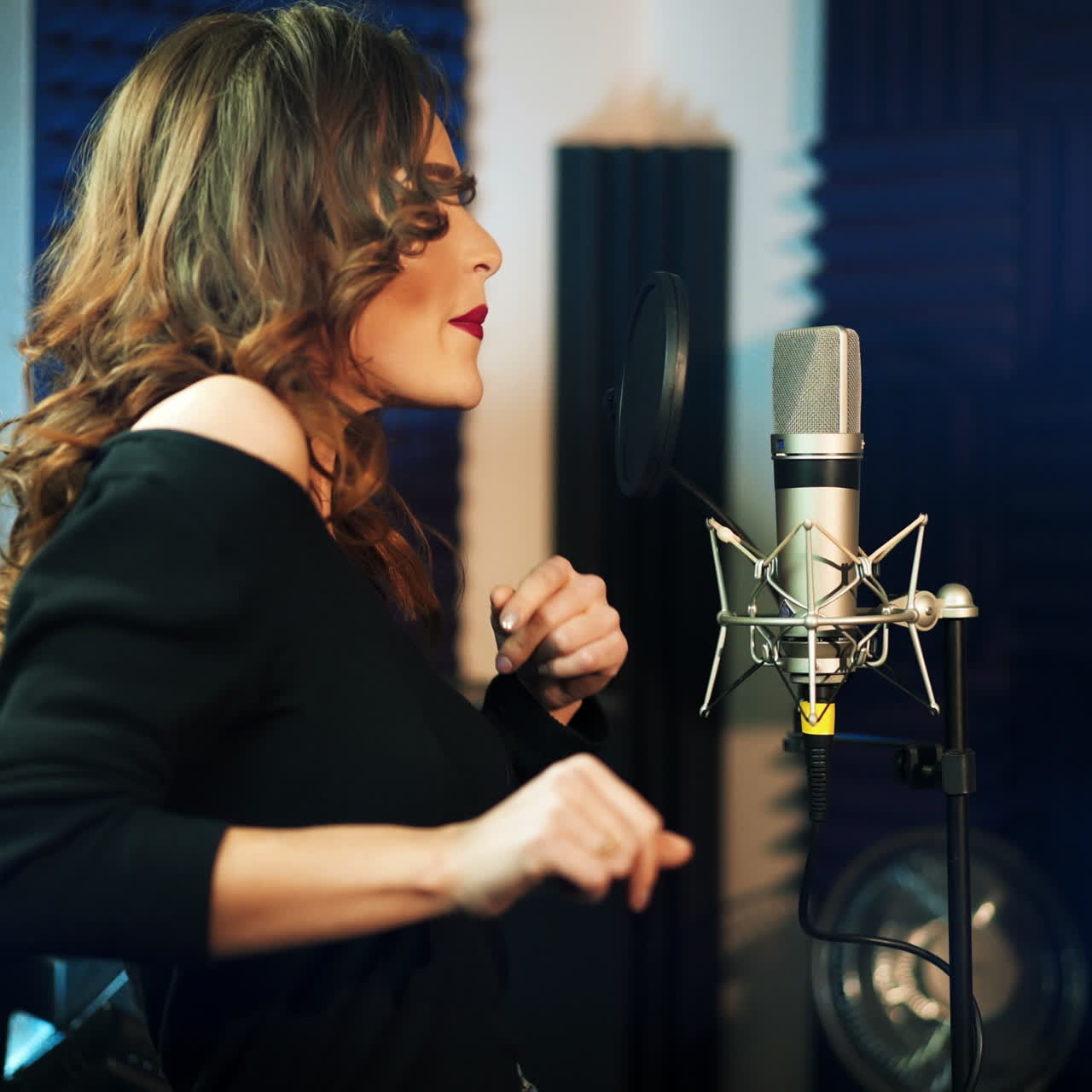 Half-length profile of a beautiful singer in the recording studio. Attractive female singing into a professional microphone and dancing gaily.