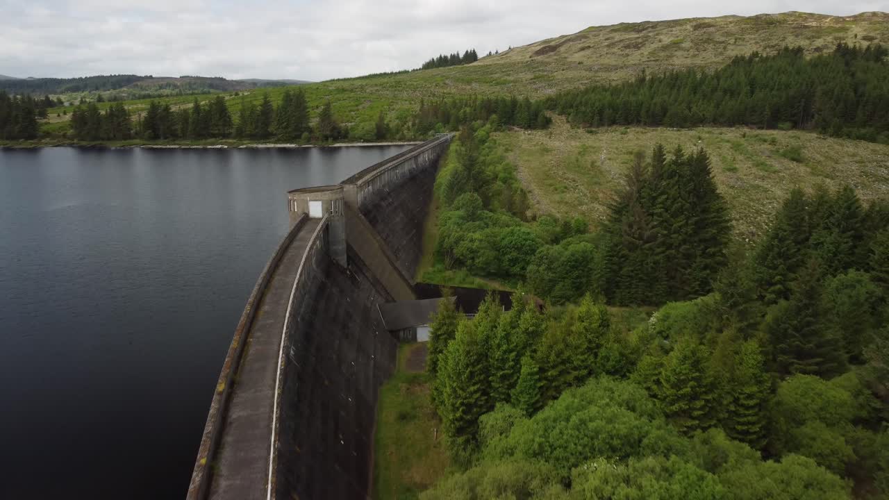 por encima de una presa de embalse rodeada de campos verdes exuberantes, árboles y colinas
