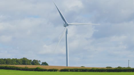 a large wind turbine spins steadily in a green agricultural field under partly cloudy skies, captured in a static wide shot with natural daylight