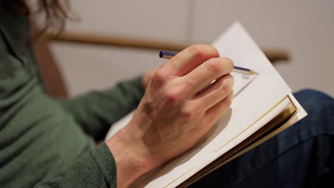 Close-up-of-artist's-hands-drawing-on-sketch-pad-with-pencil-while-sitting-on-brown-couch