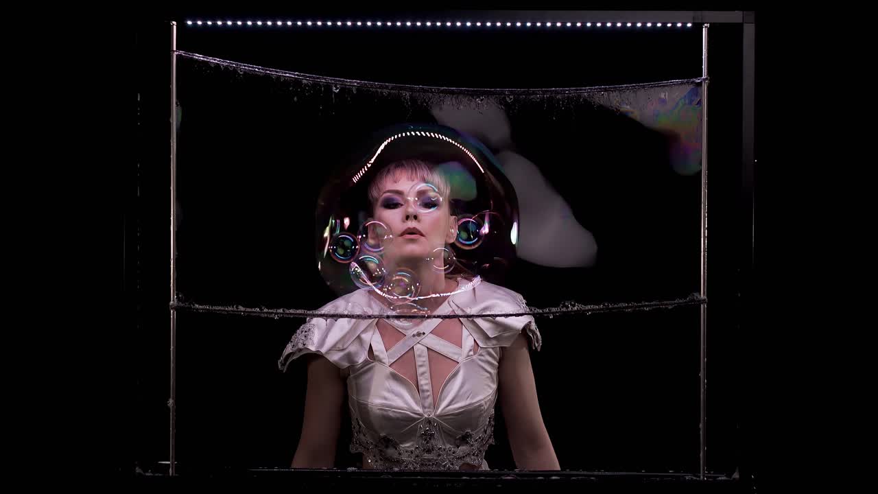 소녀는 수직 프레임의 비누 벽을 통해 많은 작은 거품을 하나의 큰 거품으로 불어냅니다.