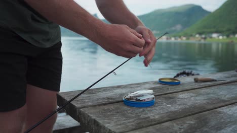 man threading bait onto hook of fishing rod by the lake shore