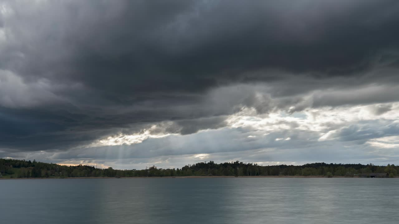 Sunbeams break through the clouds and shine on the natural landscape. Stormy clouds drift over the lake in spring, and rain is approaching. The clouds are dark and swirling.