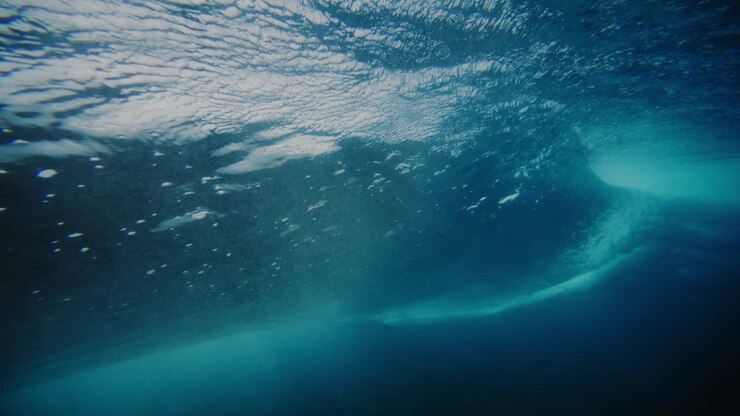 Des eaux d'un bleu profond et sombre se dressent en un tube texturé tandis qu'un surfeur effectue un cut-back à Cloudbreak, Fidji.