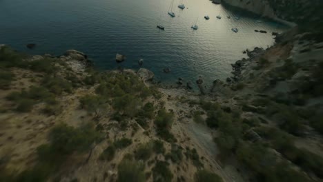 FPV-Aerial-drone-forward-moving-shot-downhill-the-green-mountain-range-along-the-seaside-in-Cala-d'Egos-beach-Mallorca,-Spain