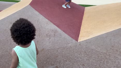 adorable y exótico niño europeo africano de dos años disfrutando en el parque infantil jugando con un coche de juguete rojo, en una calurosa tarde de verano