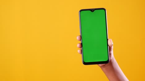 hand holding a smartphone with a green screen against a yellow background
