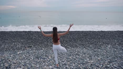 woman practicing yoga on a pebble beach by the ocean