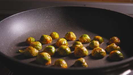 un primer plano de una mano que coloca espaciosamente coles de bruselas sazonadas y cortadas en una superficie caliente de una sartén de cerámica, el chef asa las verduras frescas como un plato saludable pero sabroso