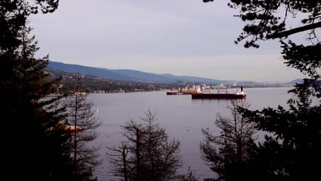 Cargo-ships-arrive-at-lit-up-Vancouver-port-in-evening,-long-shot