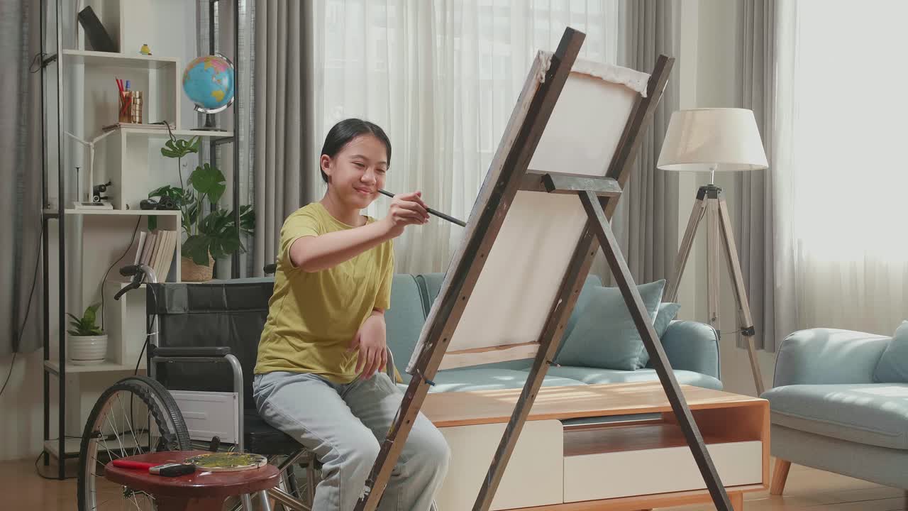 Asian Artist Girl In Wheelchair Holding Paintbrush Mixed Colour And Painting On The Canvas