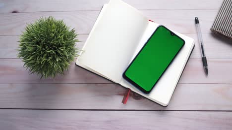 open notebook with phone and plant on a wooden desk