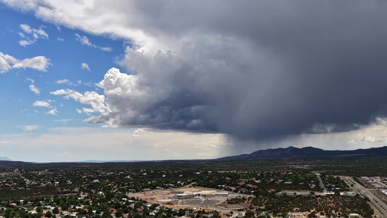 Un timelapse con drone che cattura una forte tempesta monsonica che si muove su un versante montuoso aspro. Il sistema meteorologico attivo si estende oltre una città suburbana del sud-ovest, evidenziando i dinamici cambiamenti climatici.