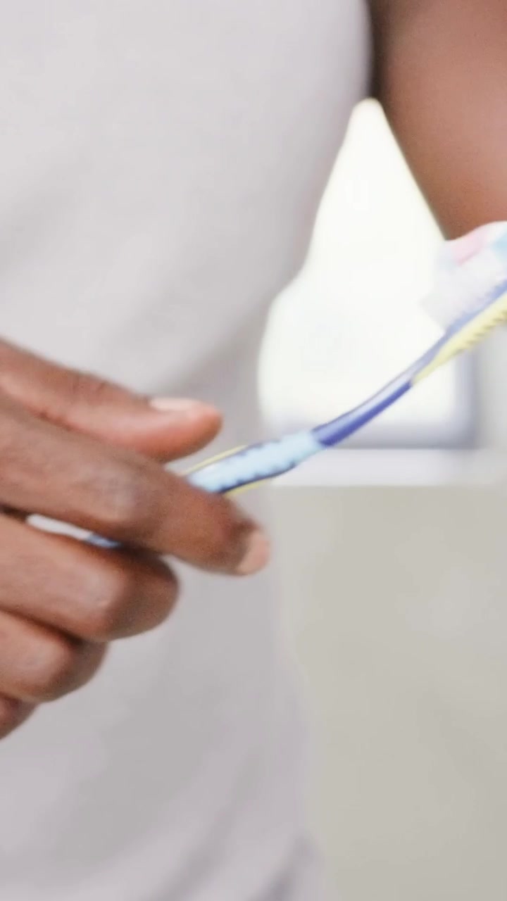 Vertical video: Aligning tube, hand pressing paste on brush at sink, preparing brush in grey shirt