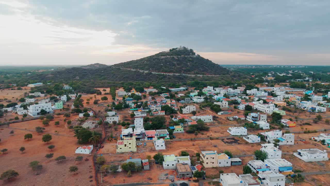 A breathtaking aerial view of a hilltop temple at sunrise, with golden rays illuminating the lush greenery, winding road, colorful houses, and serene surroundings, creating a captivating travel scene