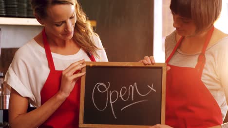 two smiling waitresses holding a open sign board