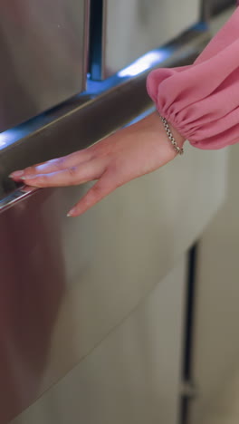 dama con vestido rosa corto cierra el cajón inferior del refrigerador iluminado por una suave luz azul en una tienda bien iluminada, su mano, adornada con un brazalete de plata, sostiene suavemente el mango