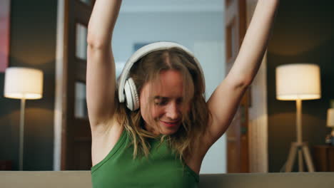 Excited-woman-dancing-indoors-sitting-sofa.-Woman-enjoying-music-moving-hands