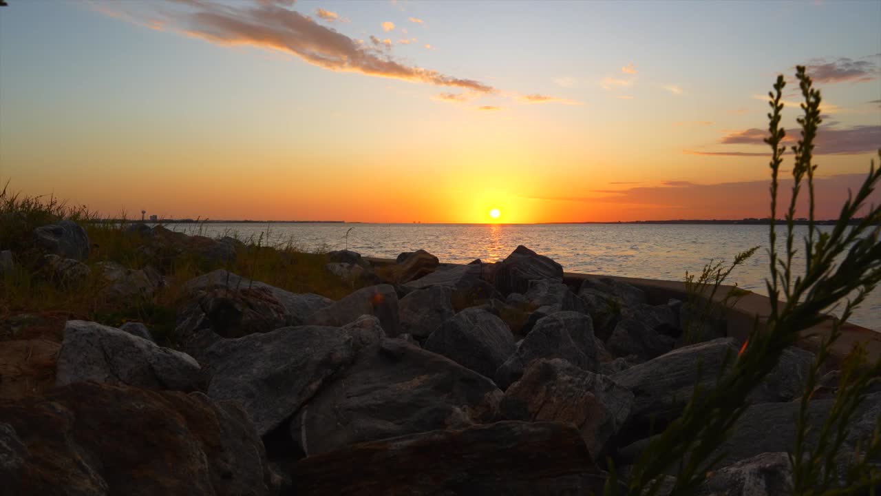 Upea Floridan auringonlasku pilkistellen rantaruohon ja suurten rantakivien välistä.