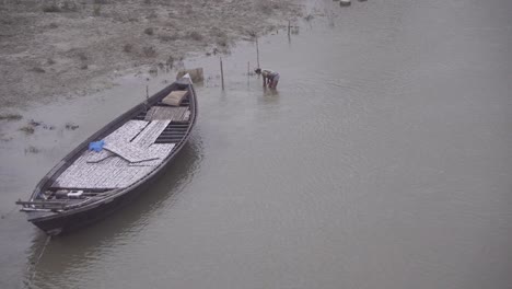 man in a river beside a boat is digging something from river bed