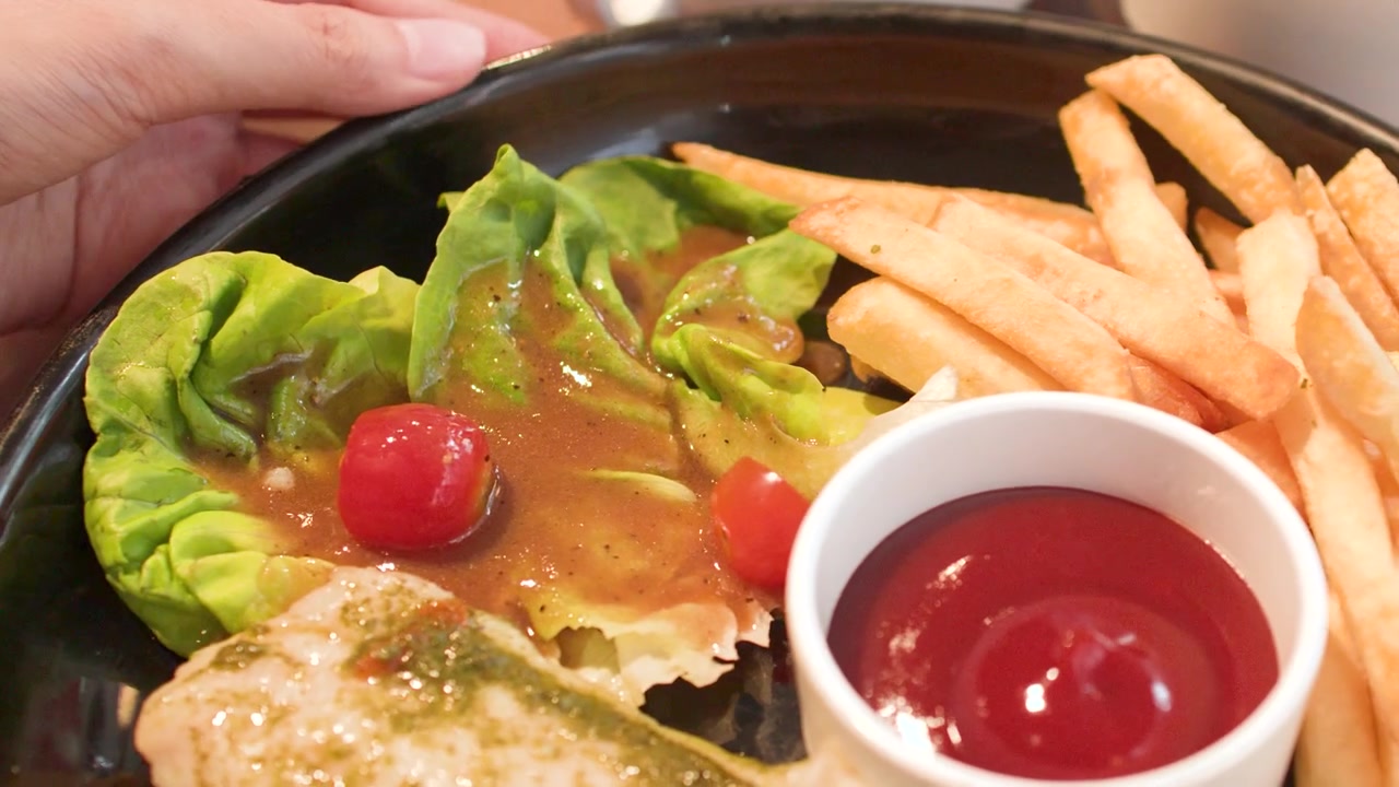 焼き魚、フライドポテト、ケチャップが乗った皿を手が回しているクローズアップショット。