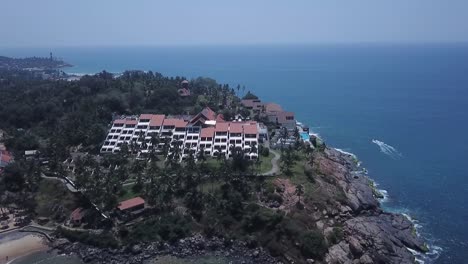Building-Exterior-Of-The-Raviz-Kovalam-Hotel-Surrounded-By-Lush-Forest-Trees-At-Kovalam-Shoreline-In-Kerala,-India---aerial-drone