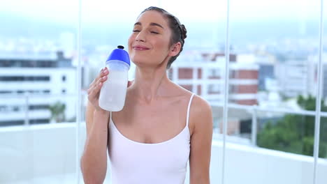 una joven sonriente bebiendo su frasco.