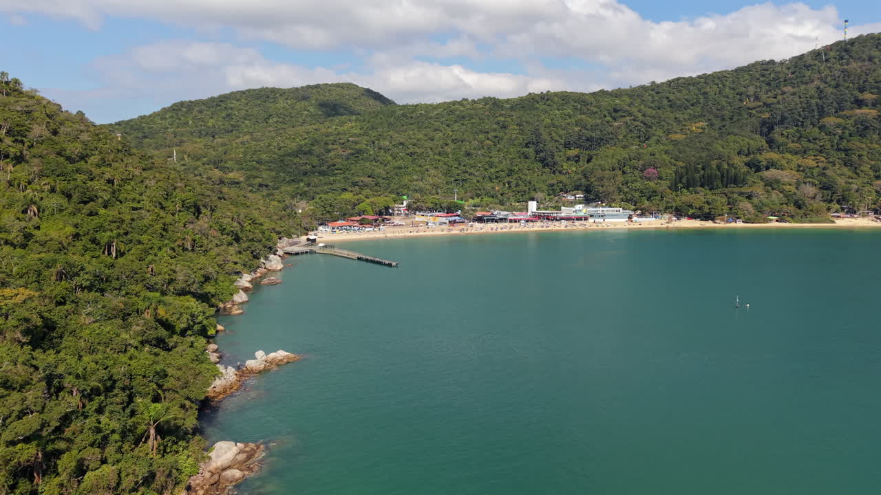 Drone shot approaching sunny beach near vegetated hills on clear early afternoon