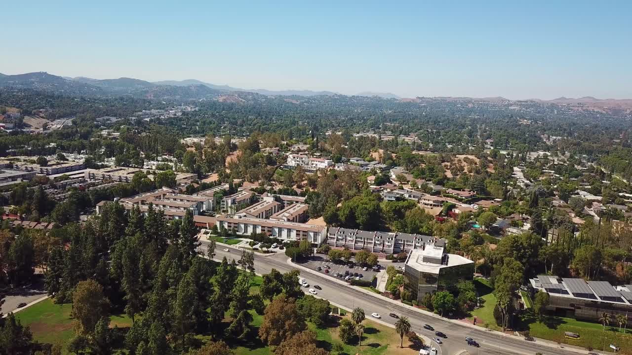 Traffic on highway in Woodland Hills Neighborhood of LA, USA. Sunny day with blue sky in fall season. Row of houses in suburbia. Aerial backwards wide shot. Los Angeles, America.