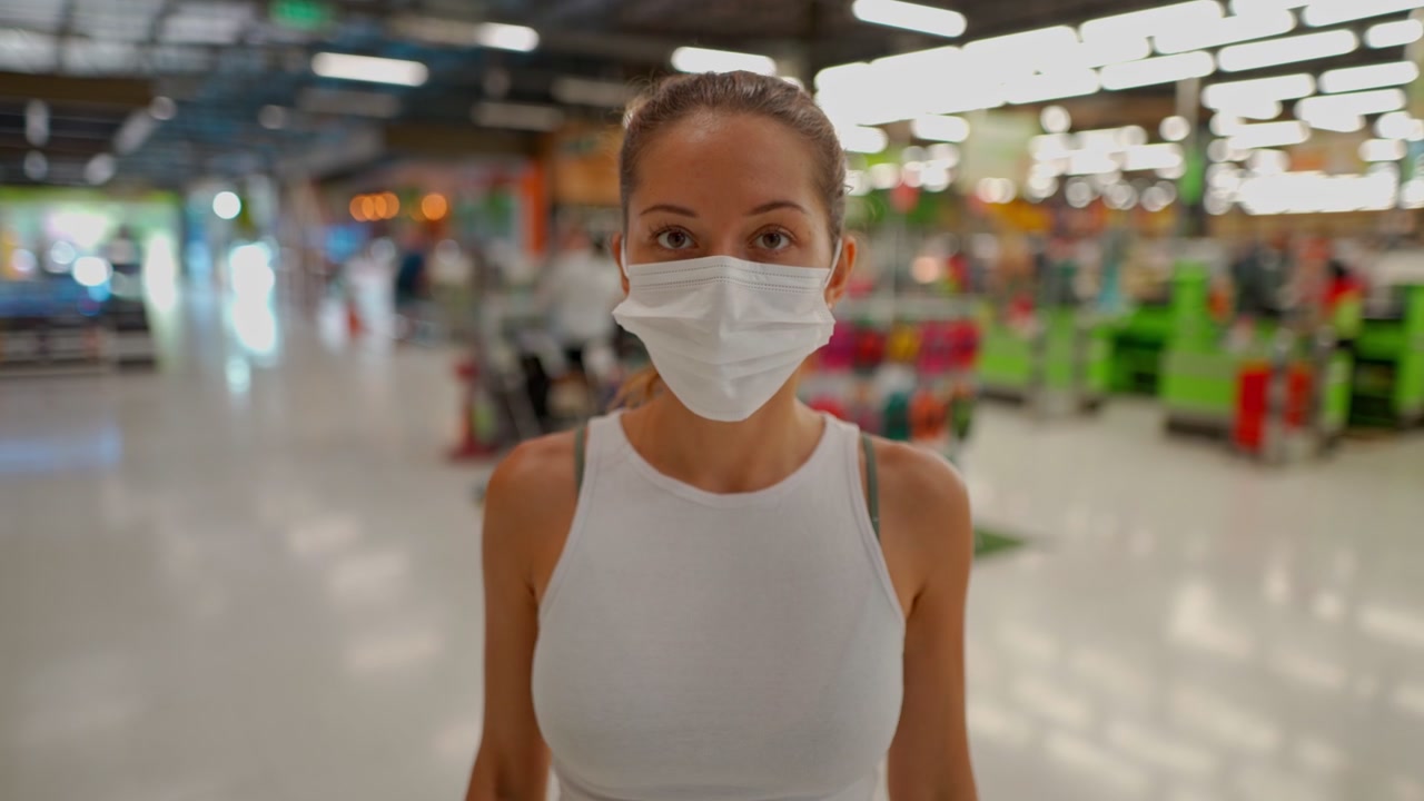 Ung kvinna sätter på sig en ansiktsmask i en stormarknad