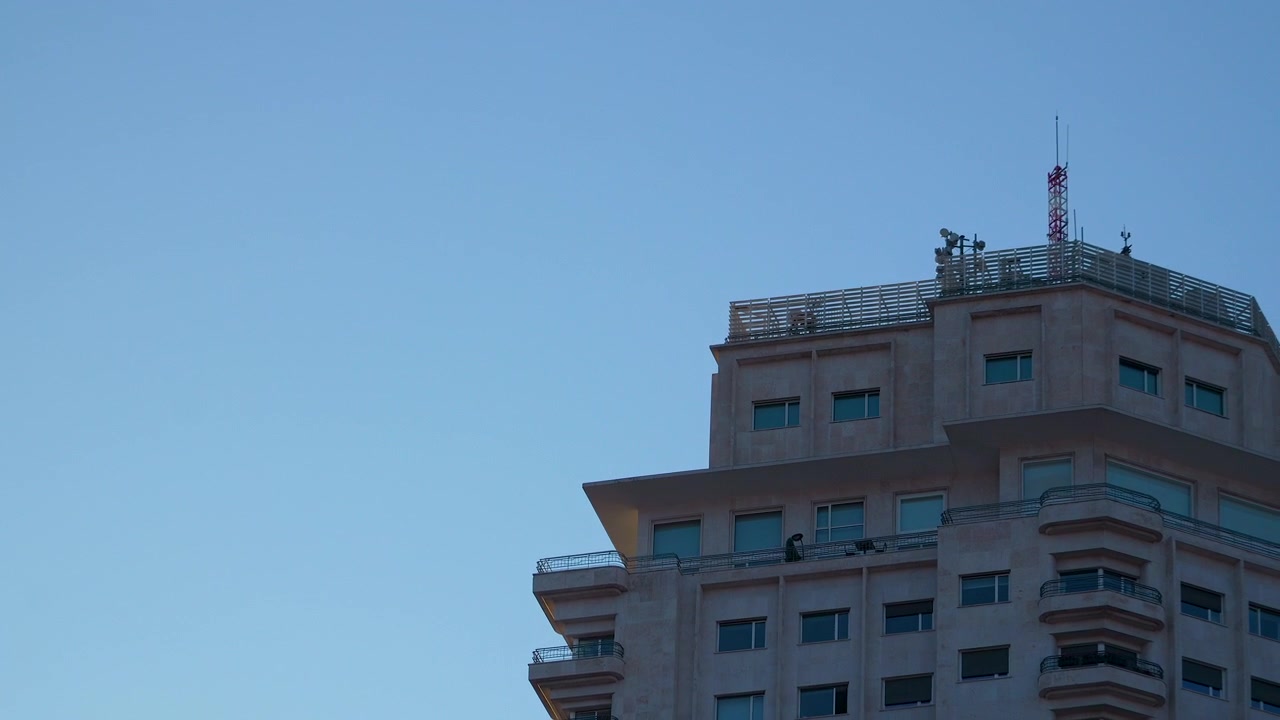 Un'inquadratura dal basso di un lussuoso edificio di appartamenti a Madrid con balconi e antenne di telecomunicazione sotto un cielo limpido al crepuscolo