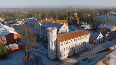 Aerial-establishing-view-of-Kuldiga-Old-Town-,-houses-with-red-roof-tiles,-sunny-winter-day,-travel-destination,-wide-drone-shot-moving-forward,-tilt-down