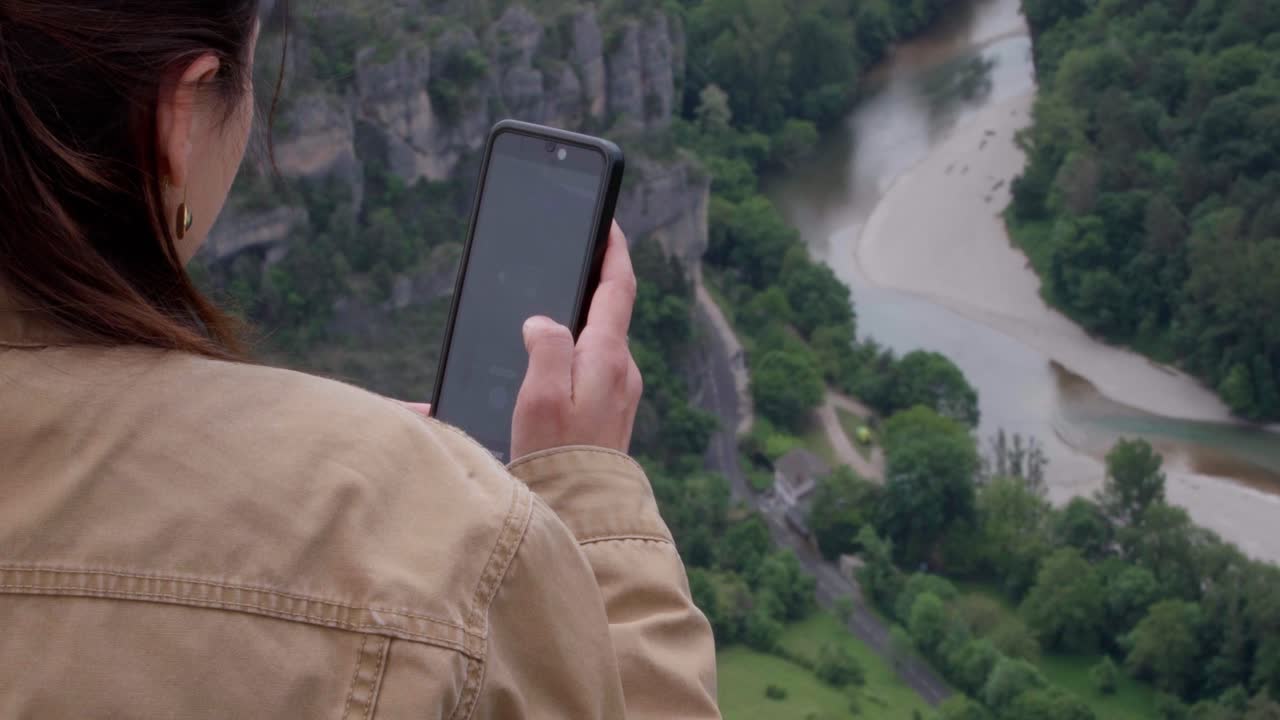A young woman uses her smartphone while overlooking le point sublime canyon.