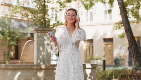 happy relaxed woman standing on city street in wireless headphones listening dancing music outdoors