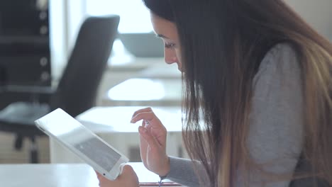 una hermosa chica sentada en la mesa de la oficina y usando su ipad.
