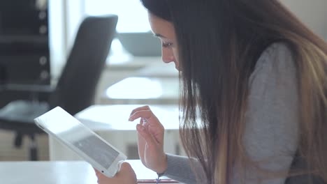 a beautiful girl sitting at the table in the office and using her ipad.