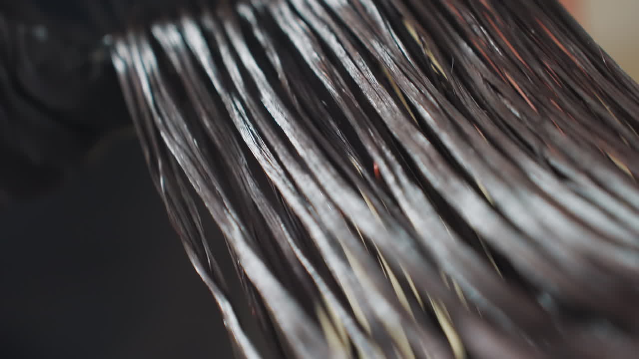 Tratamiento capilar para un pelo brillante, producto aplicado sobre el pelo húmedo en primer plano; la iluminación del salón realza la textura del pelo mojado y el efecto brillante, vista detallada del proceso de brillo capilar bajo la iluminación profesional del salón