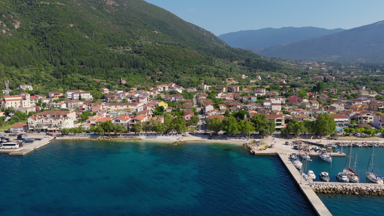 Aerial pullback shot reveals Sami town and port surrounded by turquoise sea, hills and mountains covered in pine trees, Kefalonia Island