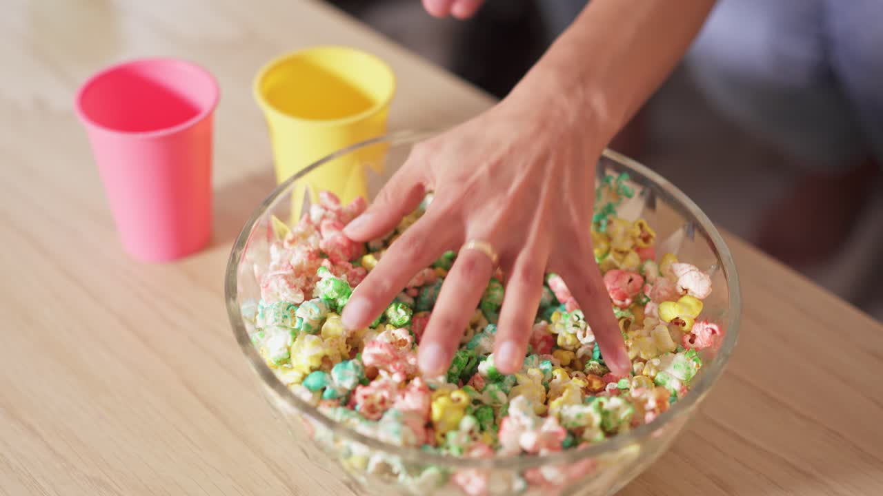 Hands Reaching for Colorful Popcorn in a Bowl