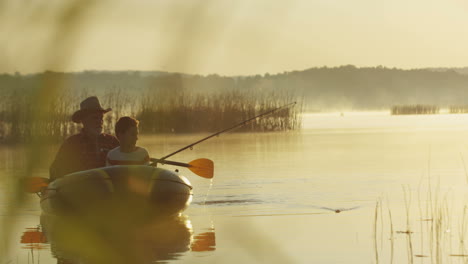 old man with a hat and his grandson on a boat fishing with a rod on the lake on a cloudy morning