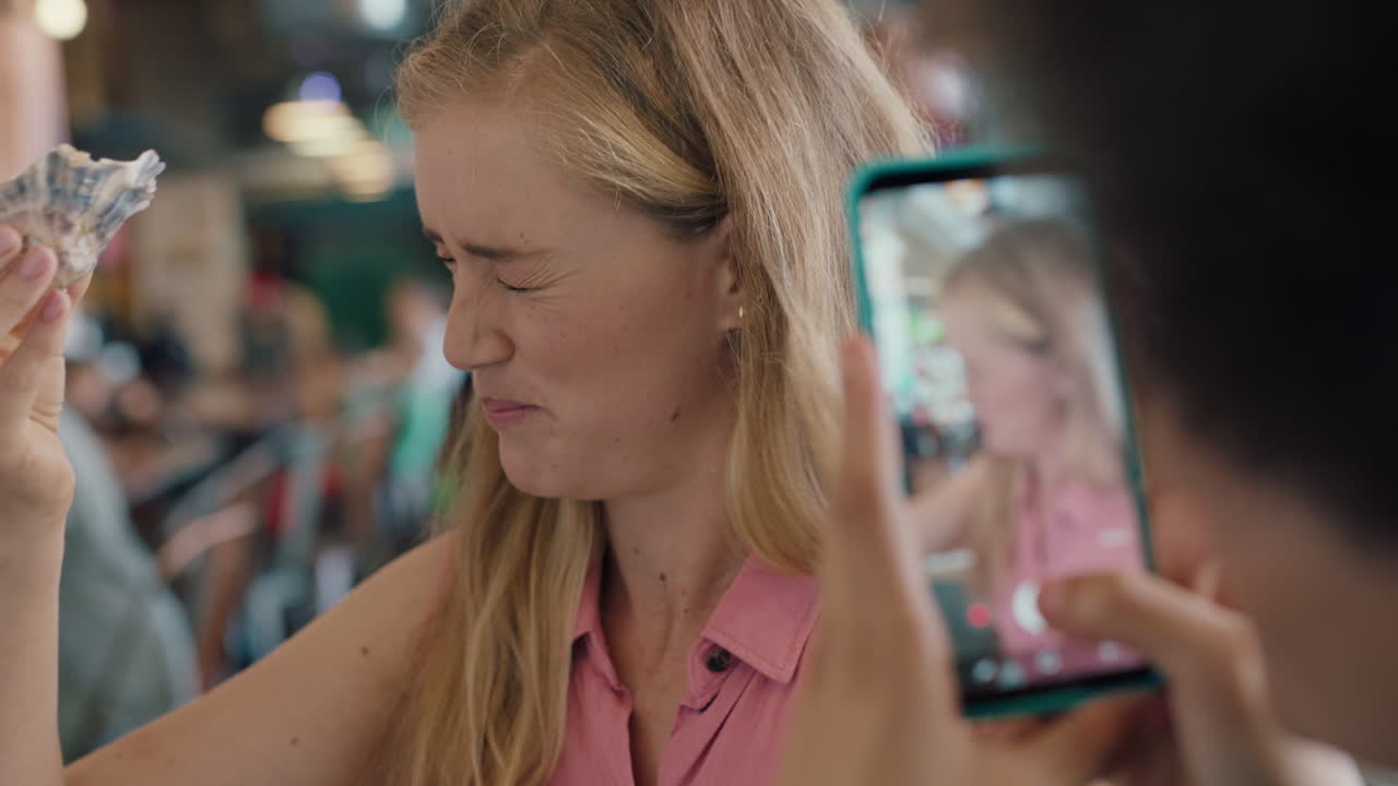 아름다운 금발 여성이 스마트폰을 사용하여 친구와 함께 레스토랑에서 굴을 먹고 즐거운 주말을 함께 소셜 미디어 4k에서 공유하는 사진을 찍습니다.