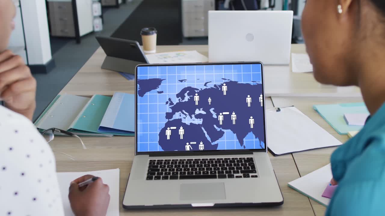 Diverse business people using laptop with digital world map and icons on screen in office
