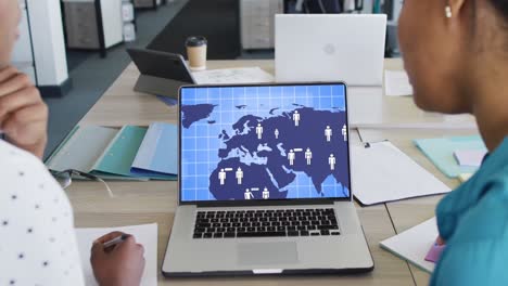 Diverse-business-people-using-laptop-with-digital-world-map-and-icons-on-screen-in-office