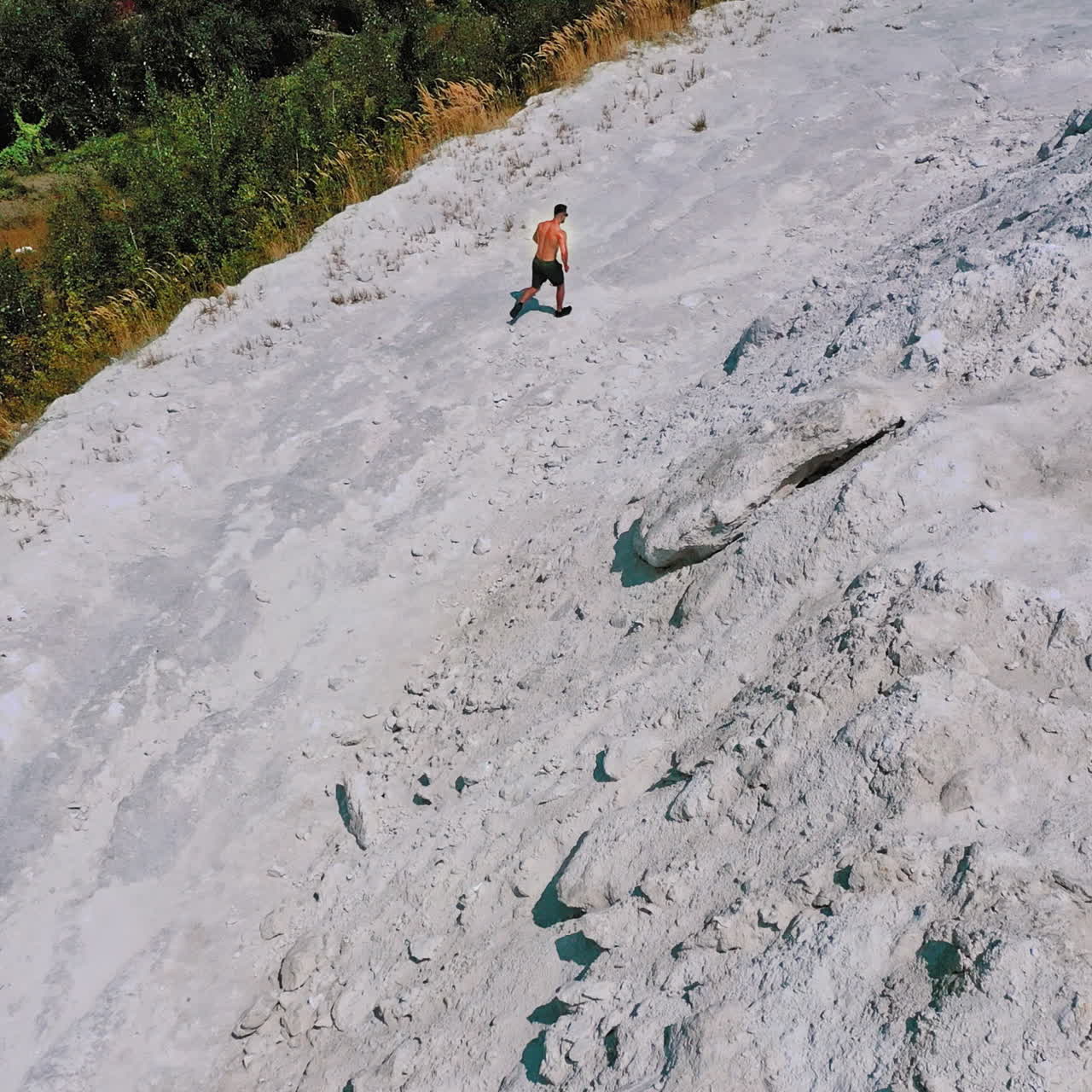 Top view on a sportsman in the mountains. Shirtless athlete is running on the white hill background in summer. Aerial view.