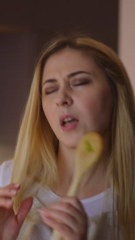 passionate blonde woman performs singing into spoon as mic and dancing while cooking festive supper in stylish kitchen at home closeup slow motion