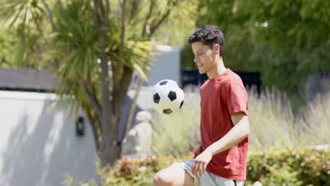 Hombre-Birracial-Enfocado-Haciendo-Malabarismos-Con-El-Fútbol-Con-Muslos-En-Un-Jardín-Soleado,-Espacio-Para-Copiar,-Cámara-Lenta